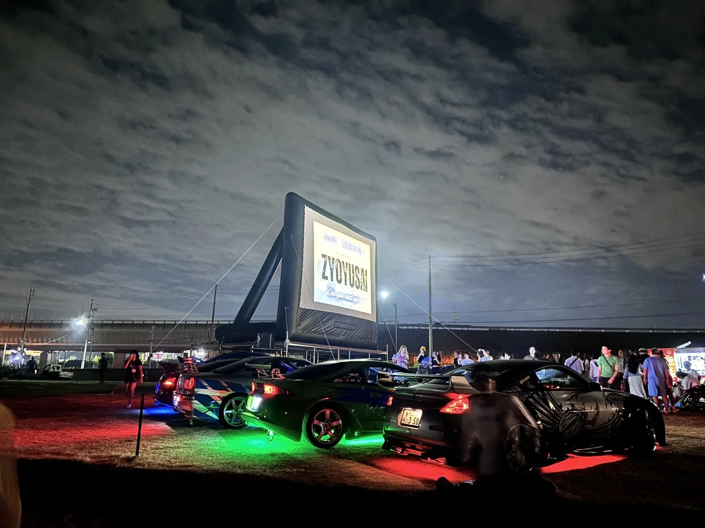 夜の屋外に立てた大型エアスクリーンと、その前に並ぶ車。